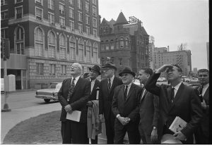 Members of the Warren Commission stand in Dealey Plaza and look up at the sixth floor of the Texas School Book Depository building in 1964.